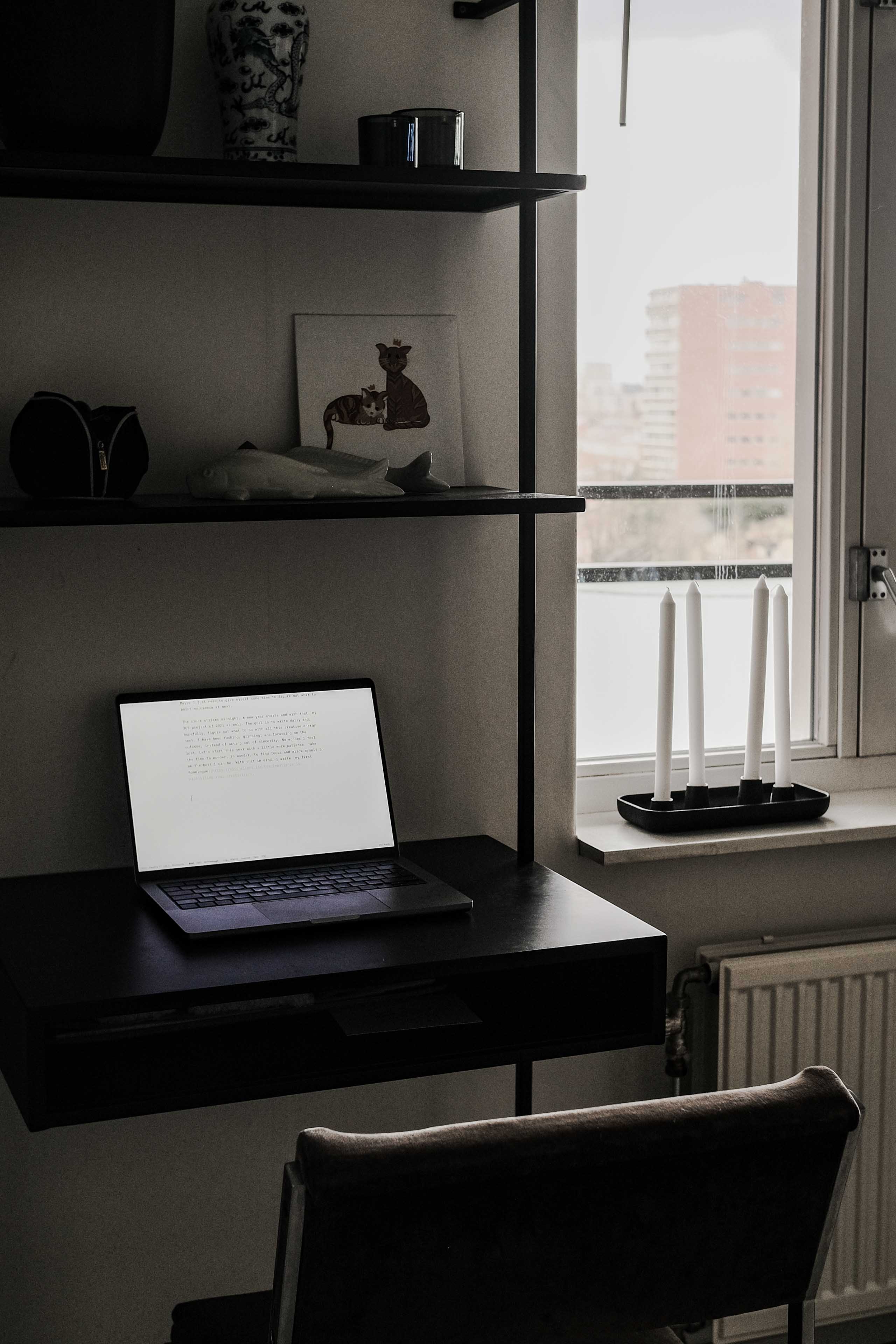 A computer on a desk, next to a window.