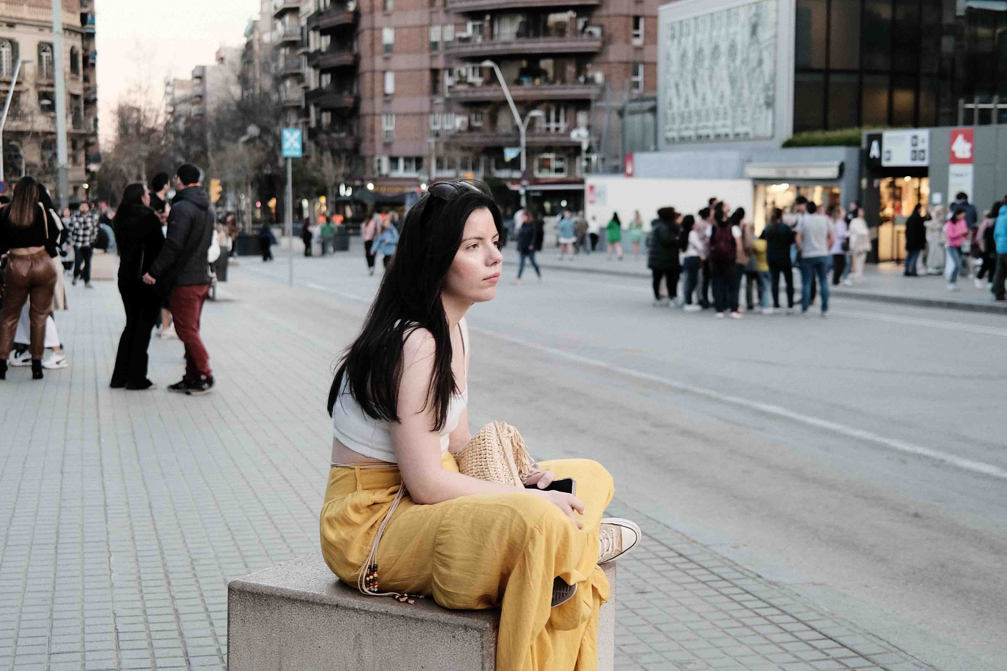 a lady sitting on a block of concrete on the sidewalk