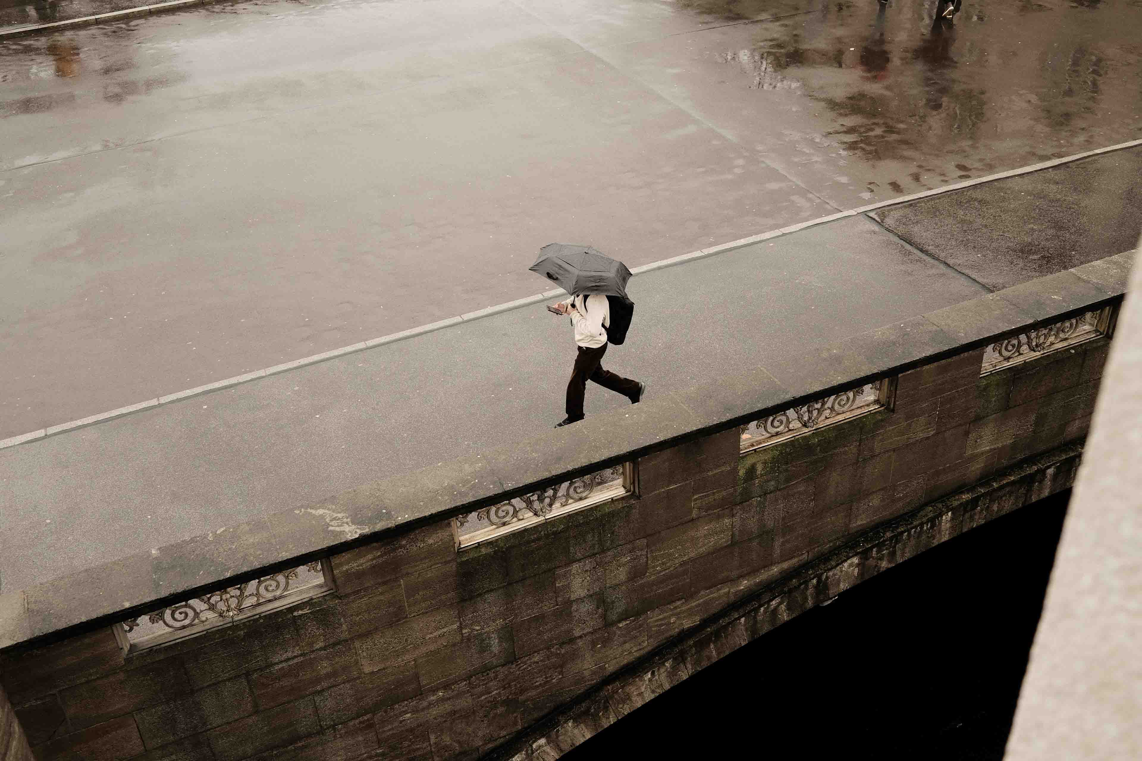 a man crossing a bridge while holding an umbrella