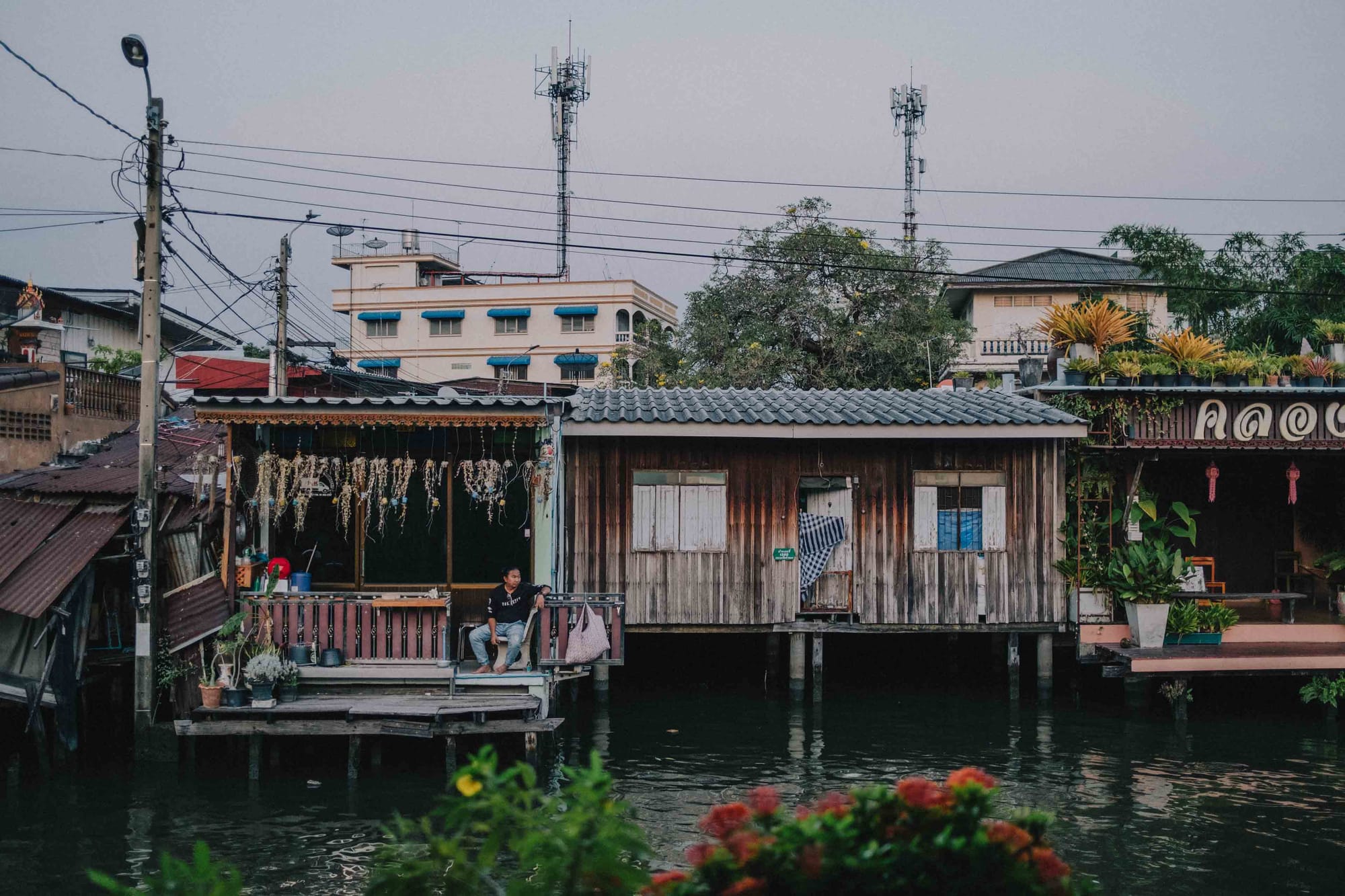A scene from Bangkok's floating markets with houses on stilts and a man sitting on his porch