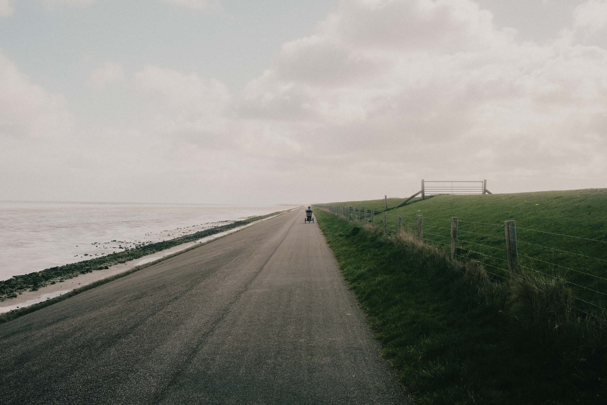 A tricycle carrying an elderly man passing on the dyke during low tide.